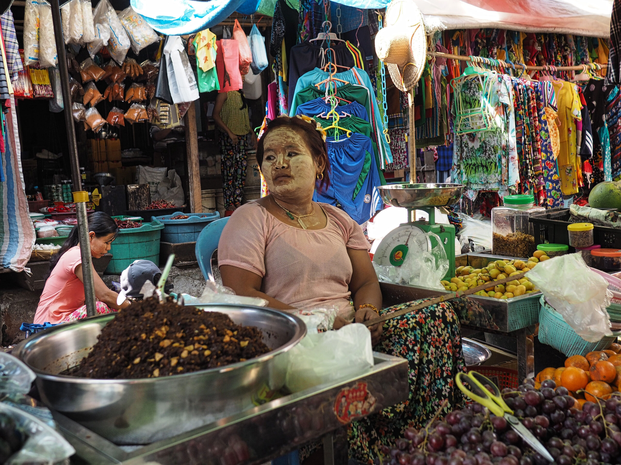 Traditioneller Markt in Myanmar mit Gemüse- und Obstständen, lokale Verkäuferin mit Thanaka-Gesichtspflege verkauft frische Früchte