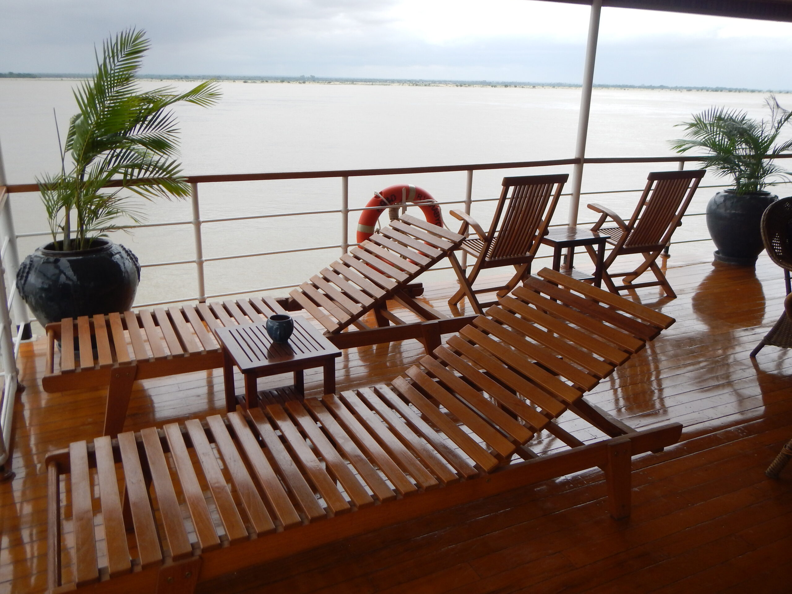 Holz-Liegestühle auf nassen Decks eines Kreuzfahrtschiffs mit Blick auf weiten Fluss und Regenwetter