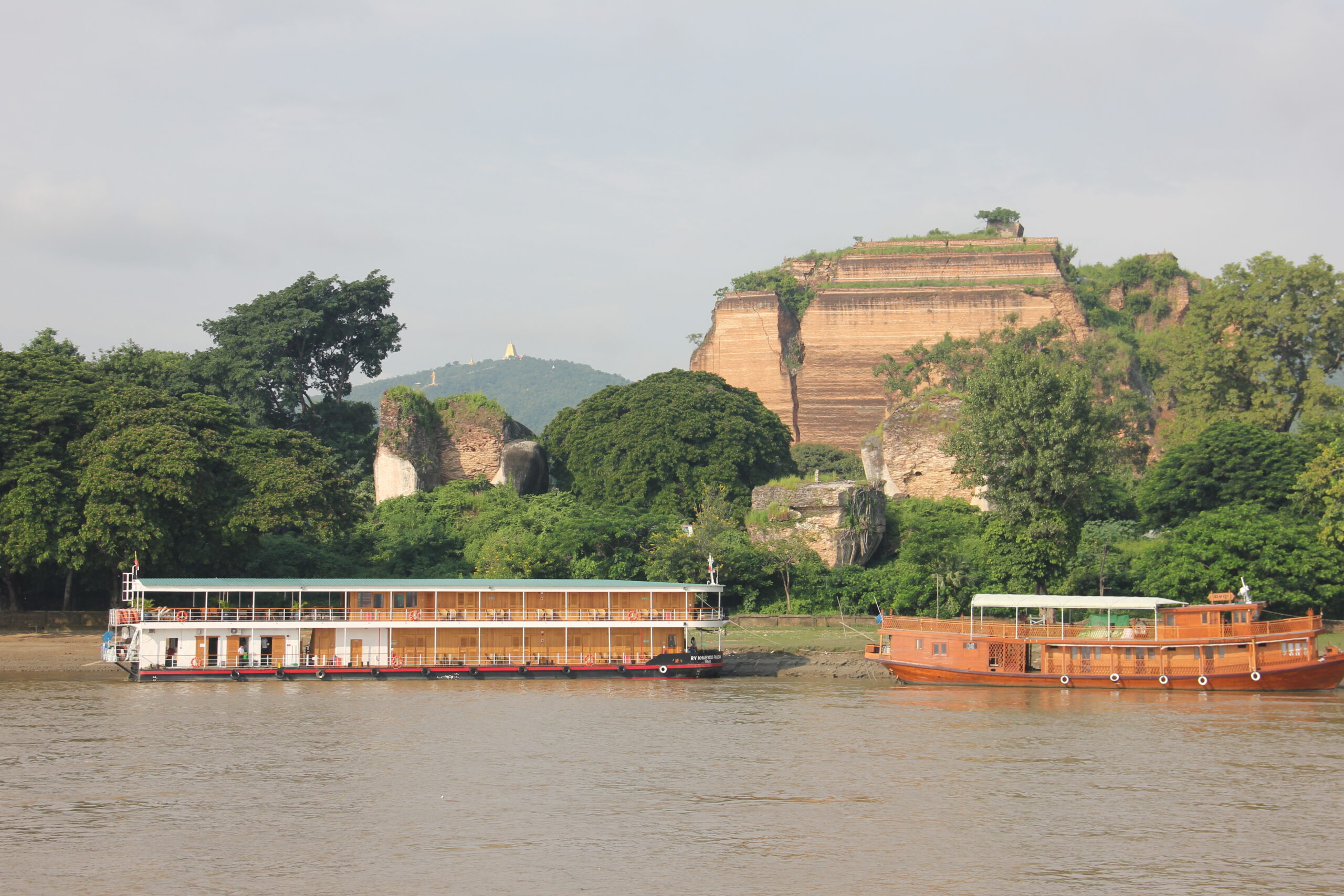 Zwei Flusskreuzfahrtschiffe am Ufer eines Flusses vor steilen Felsklippen und grüner Vegetation, in Myanmar